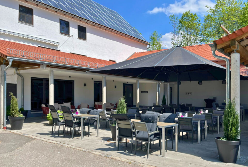 Terrasse mit schwarzen Stülen unter einem schwarzen Sonnenschirm. Am Haus im Hintergrund sieht man die neuen Fenster.